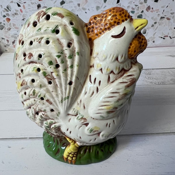 Decorative ceramic chicken figurine on a white surface with a speckled tile background