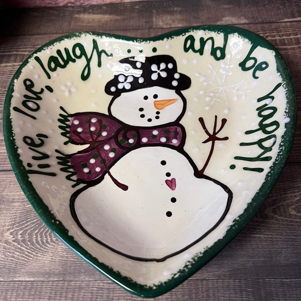 Heart-shaped plate with a snowman design and motivational text on a wooden surface