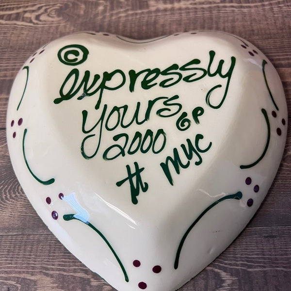 Heart-shaped ceramic item with decorative text on a wooden surface