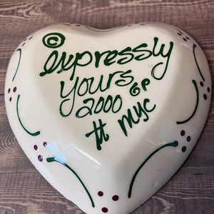 Heart-shaped ceramic item with decorative text on a wooden surface