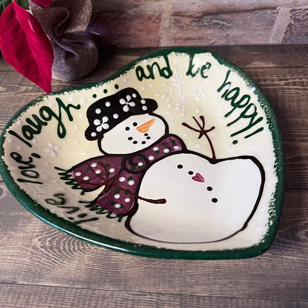 Decorative plate with a snowman design and text on a wooden surface
