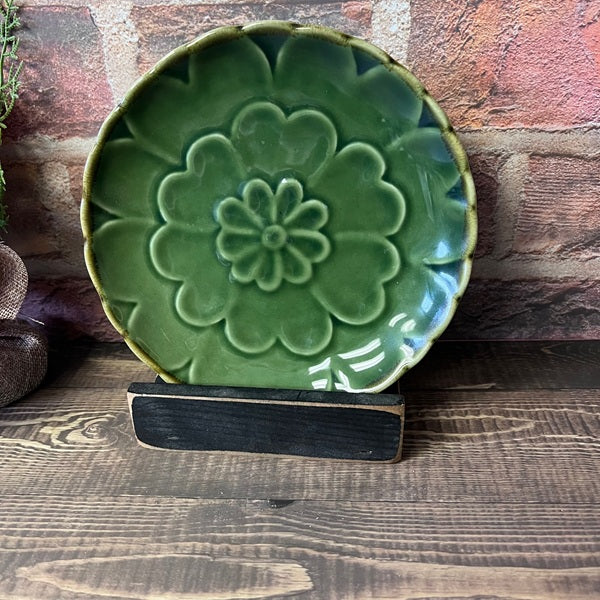 Green ceramic plate with floral design on a wooden stand against a stone wall background