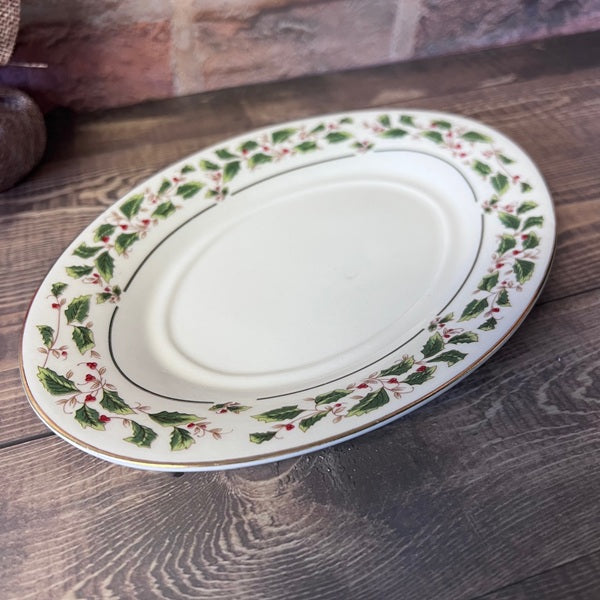 Oval ceramic platter with holly design on a wooden surface