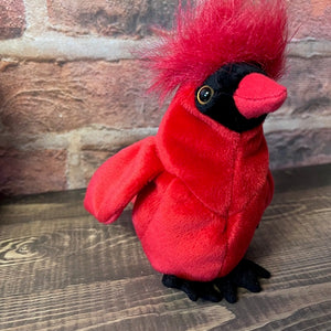 Red plush cardinal bird on a wooden surface with a brick wall background