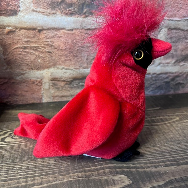 Red plush cardinal bird on a wooden surface with a brick wall background