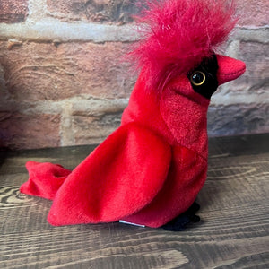 Red plush cardinal bird on a wooden surface with a brick wall background