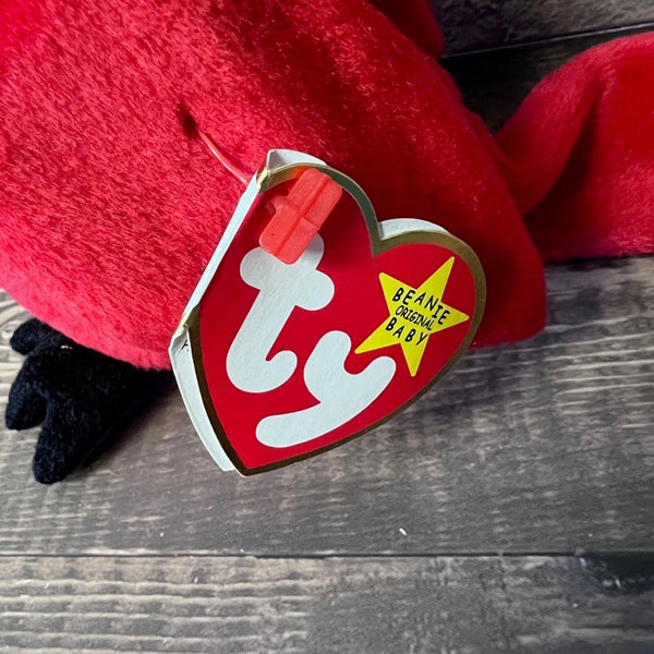 Red plush toy with a 'Beanie Baby' tag on a wooden surface