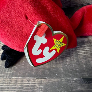 Red plush toy with a 'Beanie Baby' tag on a wooden surface
