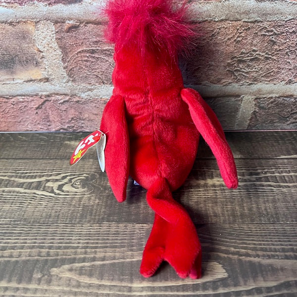 Red plush toy with a TY tag on a wooden surface and stone wall background