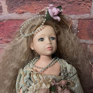 Doll with long hair, floral headband, and pearl necklace against a brick wall.