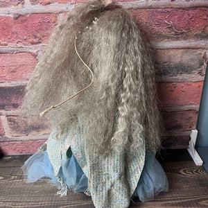 Vintage-style doll with long hair and a blue dress against a brick wall.