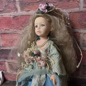 Doll with long hair and floral crown against a brick wall