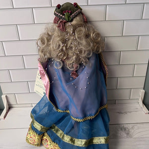 Decorative doll with a blue dress and curly hair against a white tiled wall.