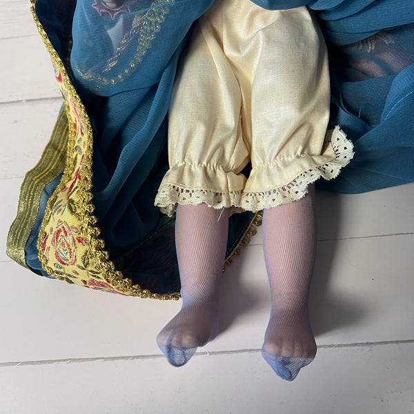 Close-up of a doll's legs wearing a yellow dress and sheer stockings on a white floor.