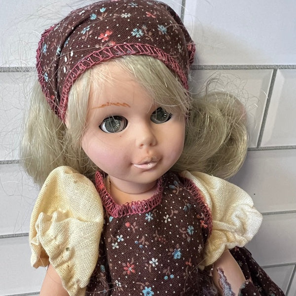 Vintage doll with floral headscarf and dress against a tiled wall background