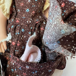 Close-up of a doll with floral-patterned dress and pink washrag in hand