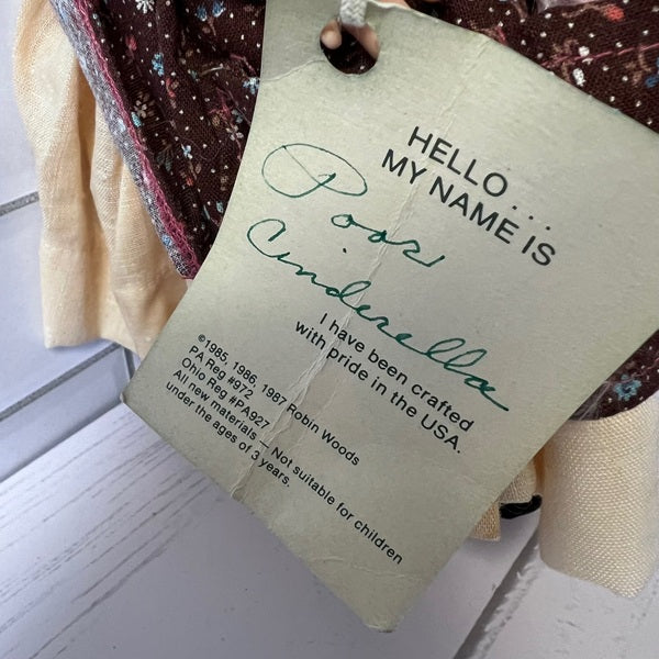 Tag on a garment with text 'Hello, my name is Poor Cinderella' and details about crafting location.