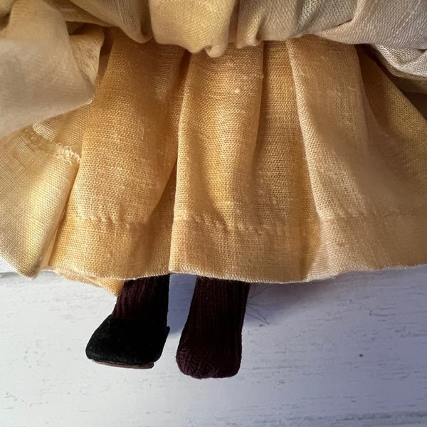 Close-up of Cinderella wearing a yellow skirt and one dark shoe on a light background