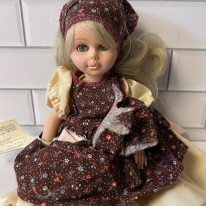 Vintage doll with a brown dress and headscarf on a white tiled wall background