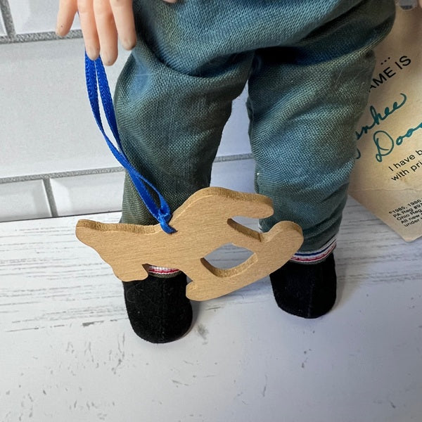 Doll wearing green pants with a wooden hand-shaped rocking horse on a blue string.