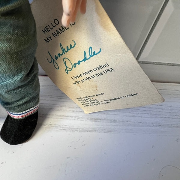 Doll holding a Yankee Doodle name with a label on a light-colored surface