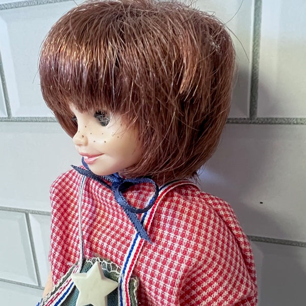 Doll with a red checkered outfit and brown hair against a tiled wall background