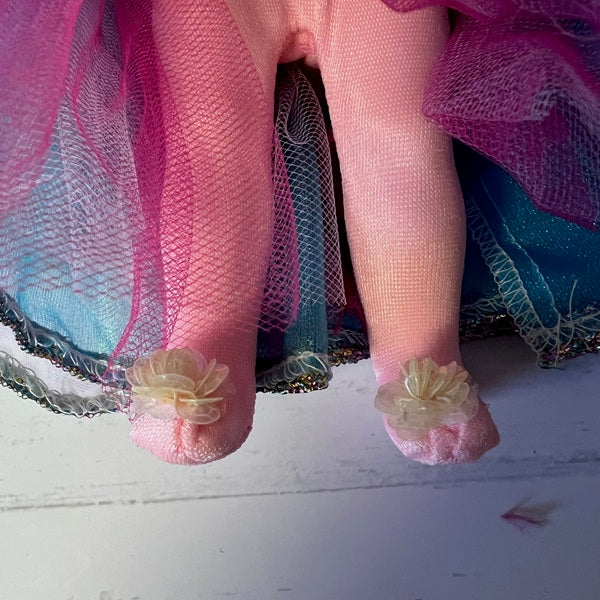 Close-up of a doll's feet with pink tights and floral decorations on a white surface.