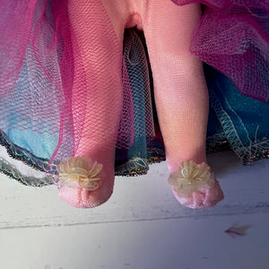 Close-up of a doll's feet with pink tights and floral decorations on a white surface.