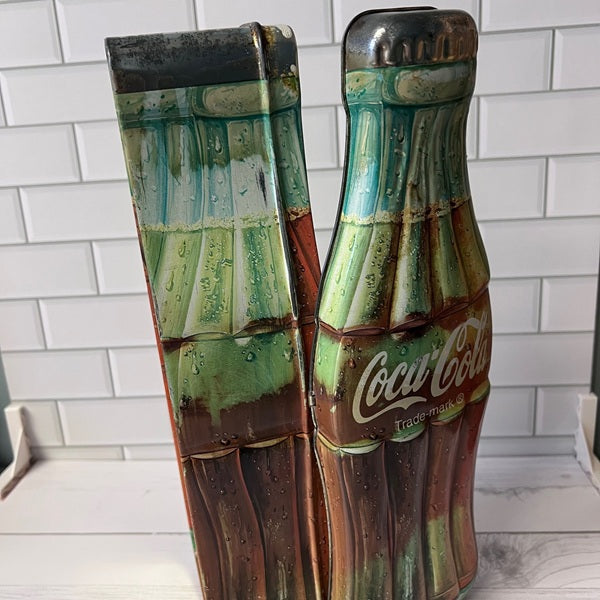 Coca-Cola bottle-shaped tin on a white tiled floor