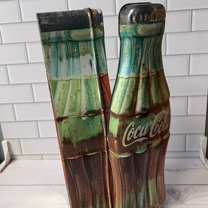 Coca-Cola bottle-shaped tin on a white tiled floor