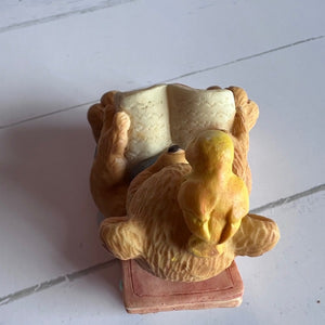 Figurine of a bear holding a book on a white surface