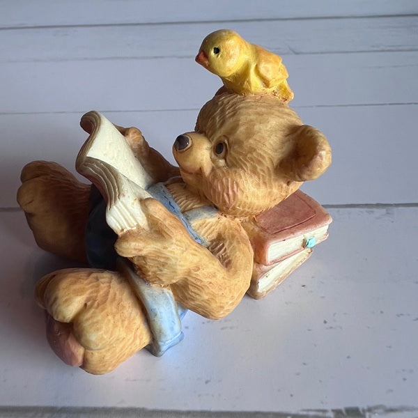Teddy bear reading a book with a bird on its head against a white background