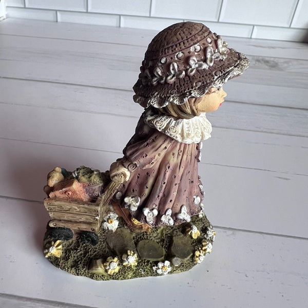 Decorative figurine of a woman with a hat and a cart on a white wooden background