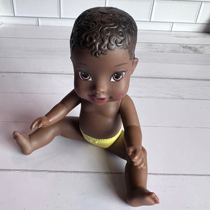 Doll with dark skin and yellow diaper on a light wooden floor