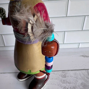 Colorful Native American figurine with beads and feathers on a white tiled background