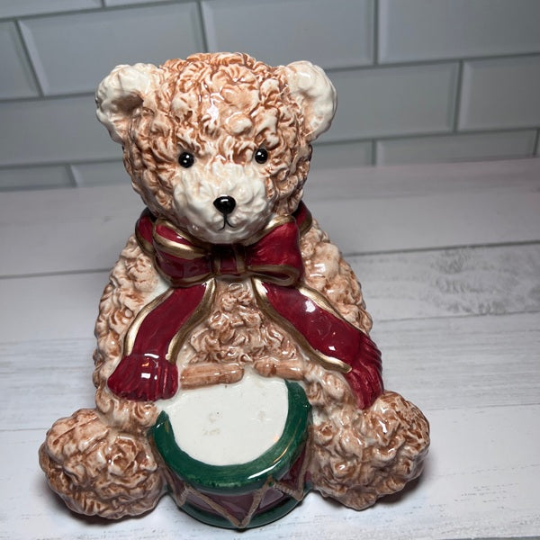 Decorative teddy bear with a red scarf and drum on a white surface.