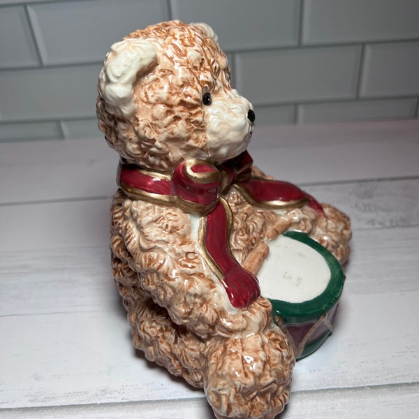 Decorative bear figurine with a red bow and drum on a white surface.