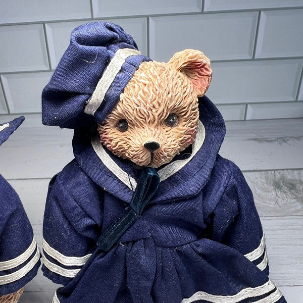 Teddy bear in a navy blue outfit with white trim on a light wooden floor.