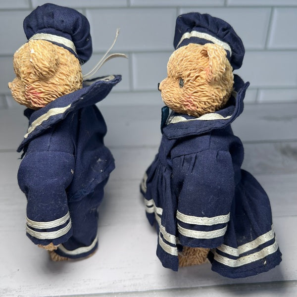 Two teddy bears in navy uniforms with white stripes on a white surface.