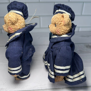 Two teddy bears in navy uniforms with white stripes on a white surface.
