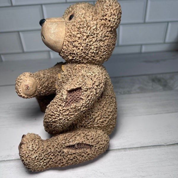 Textured teddy bear sitting on a wooden surface with a white tiled wall background