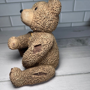Textured teddy bear sitting on a wooden surface with a white tiled wall background