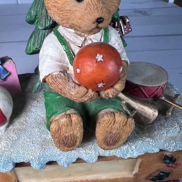 Decorative figurine of a bear holding a ball with a Christmas tree and drum in the background.