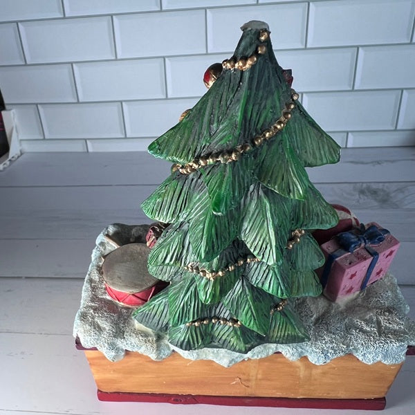 Decorative Christmas tree figurine with presents on a white tiled wall background