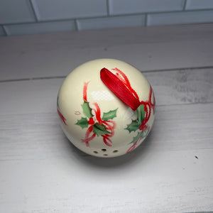 Decorative ceramic ball with red ribbon and green leaves on a white surface.