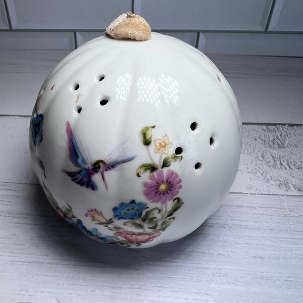 Decorative ceramic ball with floral designs and a bird on a white surface.