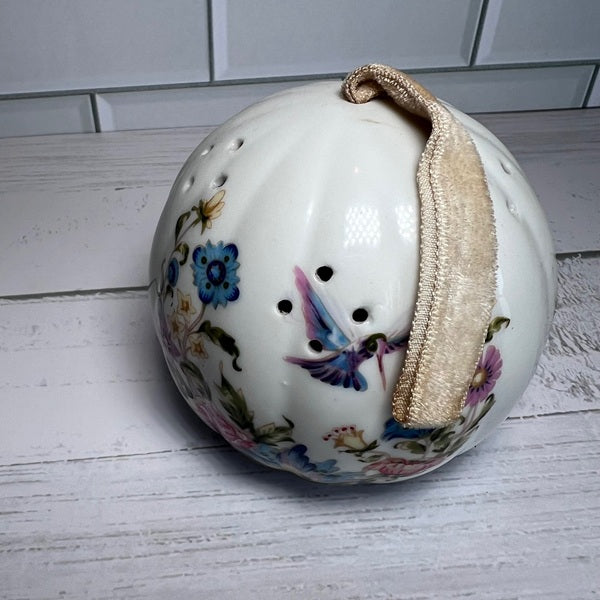 Decorative ceramic ball with floral and butterfly designs on a white wooden surface.