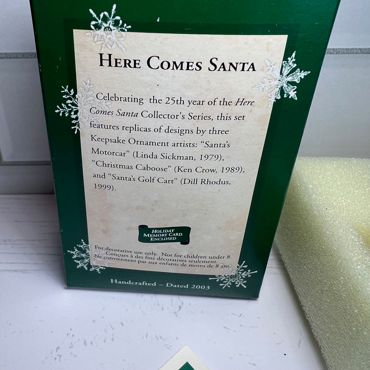 Decorative packaging for a 'Here Comes Santa' collectible set with text and green border.