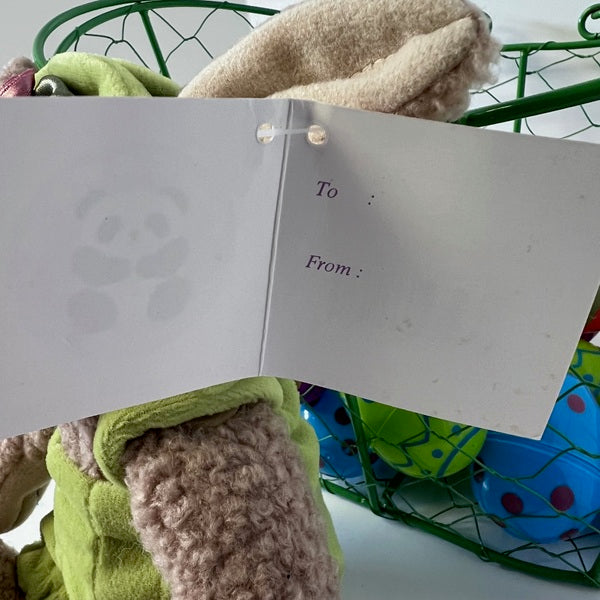Open card with 'To' and 'From' fields held by plush toys in a green basket.