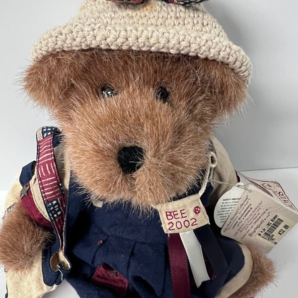 Teddy bear wearing a knitted hat and outfit with visible brand tag on a white background
